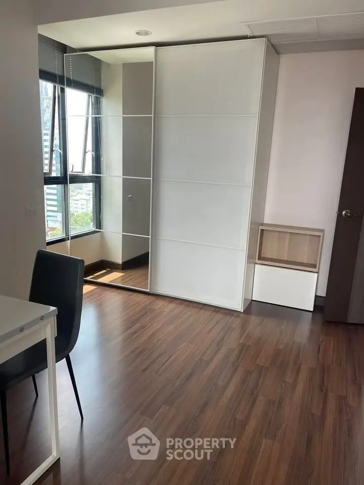 Modern apartment interior with wooden flooring and large window, featuring a sleek wardrobe and stylish chair.