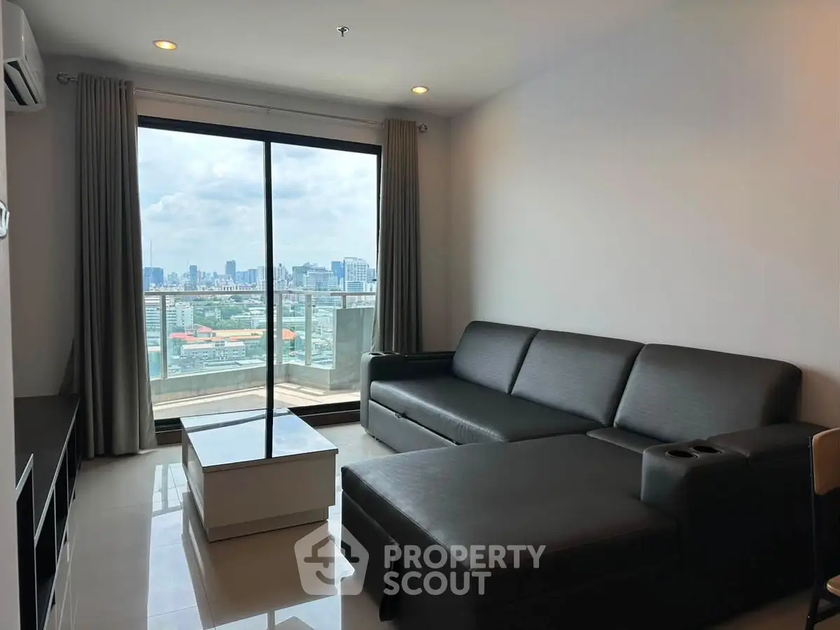 Modern living room with city view, featuring sleek black sofa and large windows for natural light.