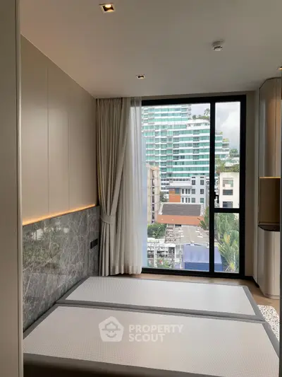 Modern bedroom with large window offering city view, featuring sleek design and natural light.