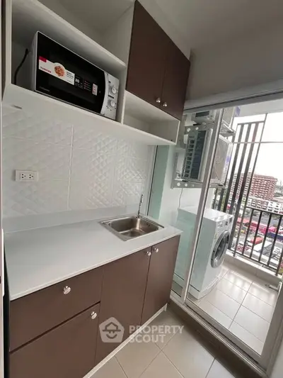 Modern compact kitchen with microwave and washing machine, featuring sleek cabinetry and balcony view.