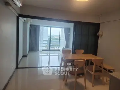 Modern dining area with wooden table and chairs, sliding glass doors leading to a balcony with a view.