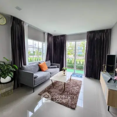 Modern living room with large windows, elegant curtains, and stylish furniture overlooking a lush garden.