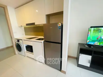 Modern compact kitchen with appliances including fridge, washing machine, and TV in cozy apartment.