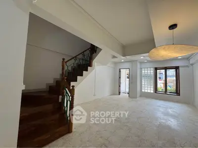 Spacious living room with elegant staircase and large window offering natural light.