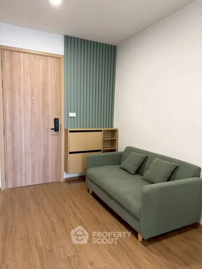 Modern living room with green sofa and wooden flooring, featuring stylish wall paneling and storage unit.