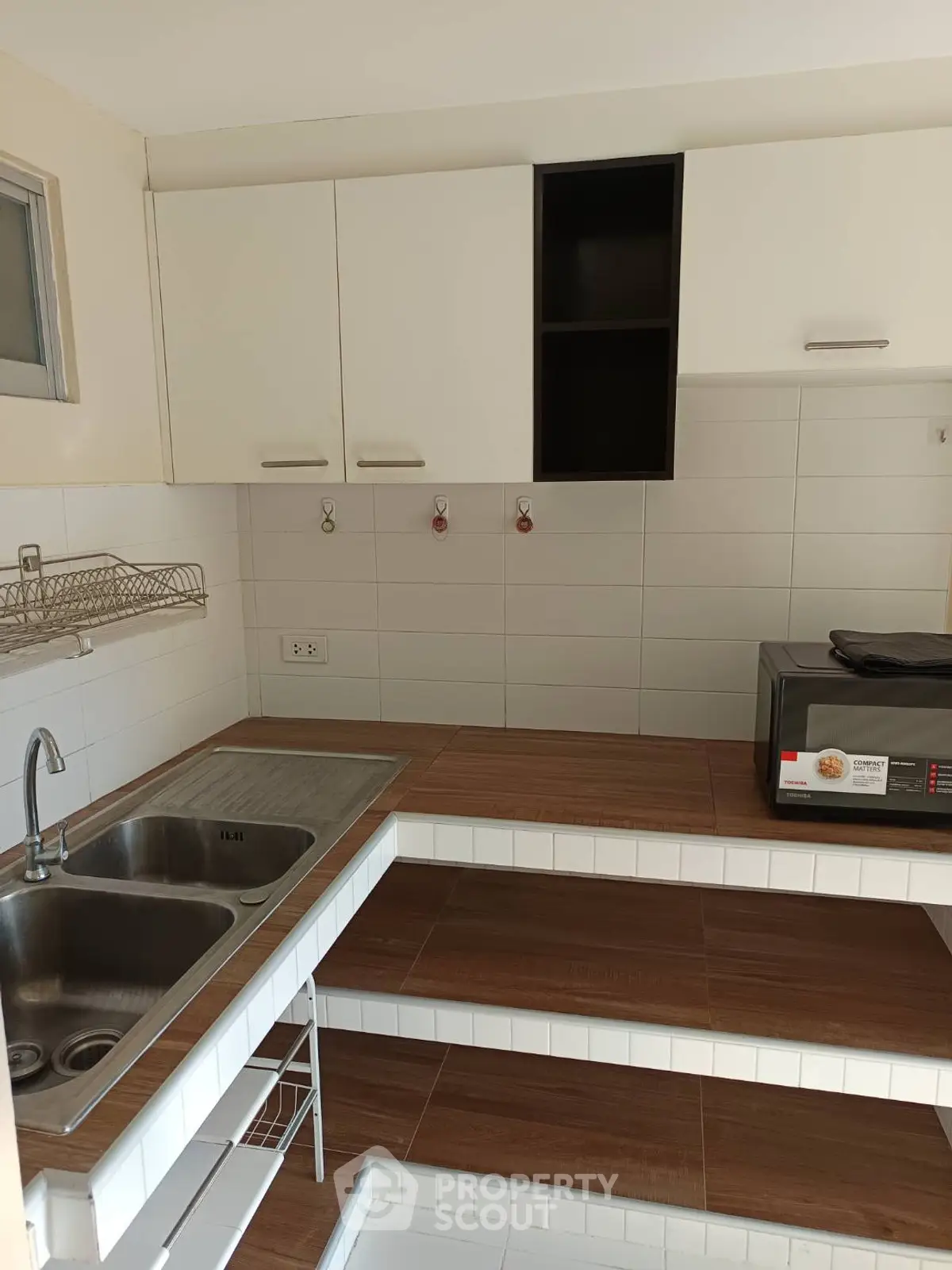 Modern kitchen with sleek cabinetry and microwave, featuring a double sink and tiled countertops.