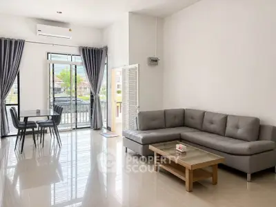 Spacious modern living room with sleek gray sofa and dining area, featuring large windows and natural light.