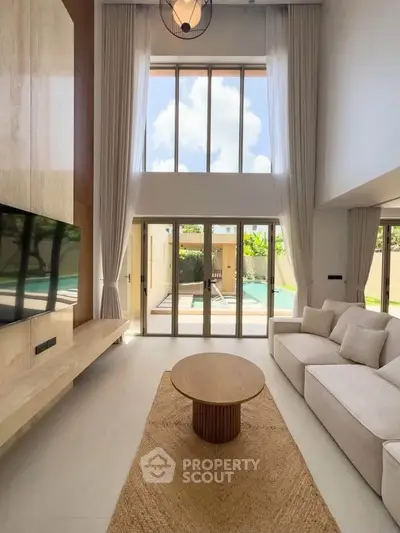 Luxurious living room with high ceilings, large windows, and pool view, featuring modern decor and natural light.