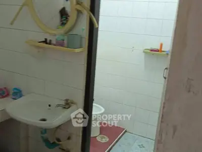 Compact bathroom with white tiles and basic fixtures, featuring a round mirror and small shelves.