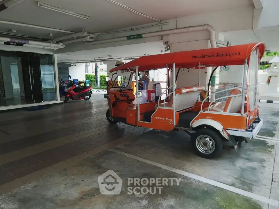 Covered parking area with tuk-tuk and motorcycles in a residential building.