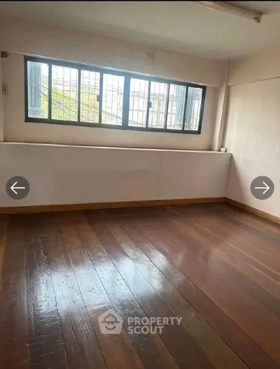 Spacious empty room with wooden flooring and large window, ideal for customization.