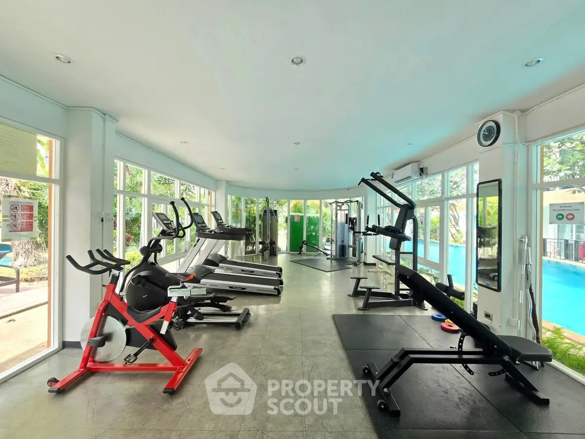 Spacious gym with modern equipment and pool view in luxury real estate property.