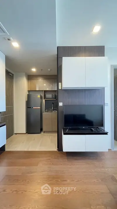 Modern apartment interior with sleek kitchen and living area featuring wood flooring and built-in cabinets.