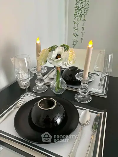 Elegant dining setup with black dinnerware, candles, and floral centerpiece on a modern table.