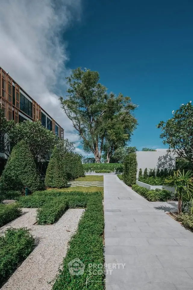 Luxurious garden pathway with lush greenery and modern architecture under a clear blue sky.