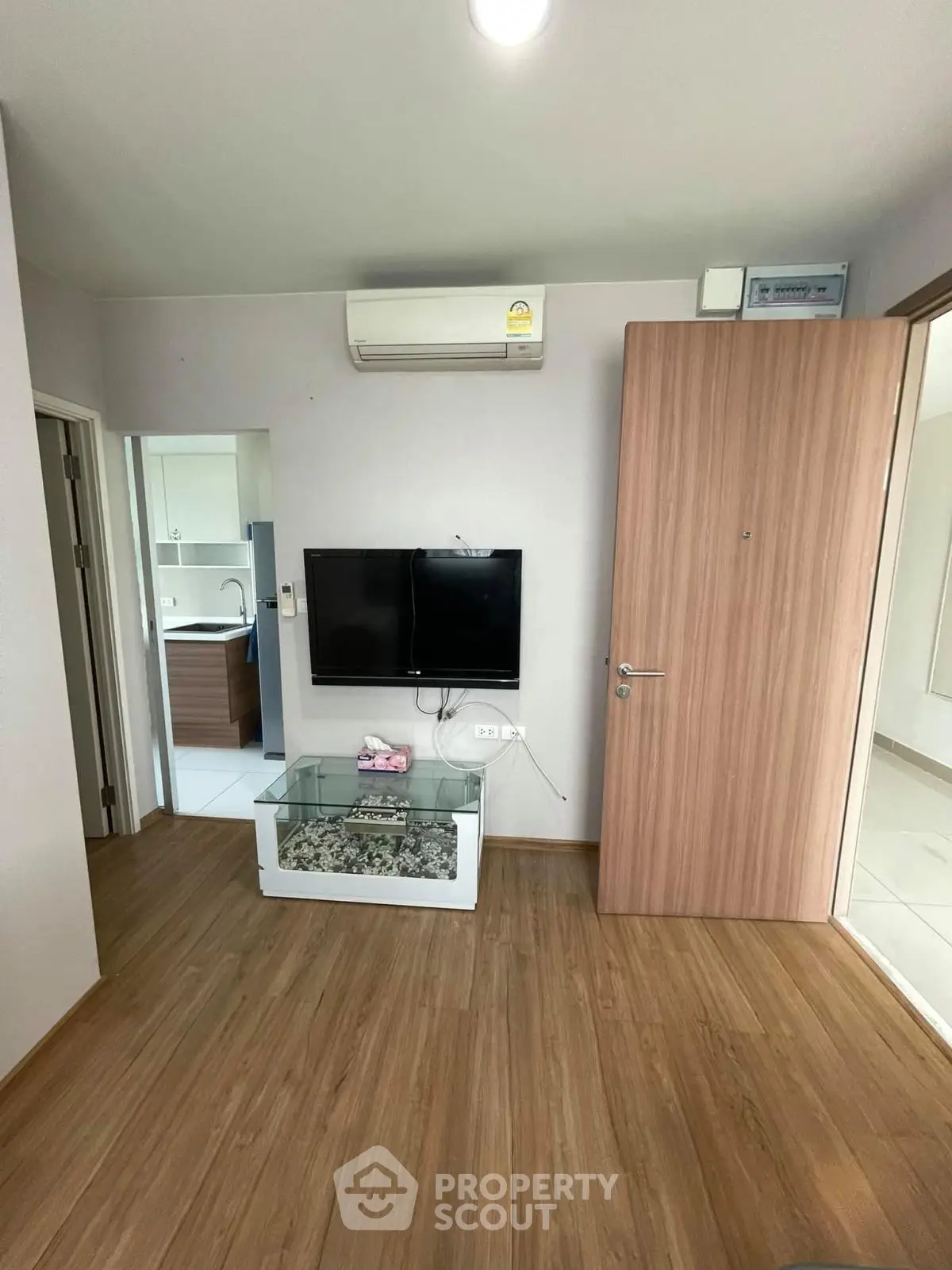 Modern living room with wooden flooring, wall-mounted TV, and air conditioning unit.