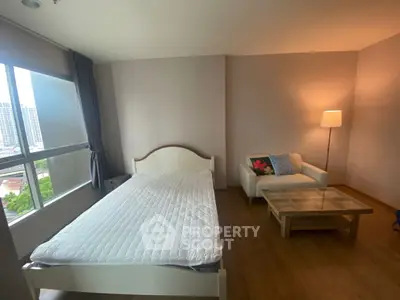 Spacious bedroom with large window and cozy seating area in modern apartment.