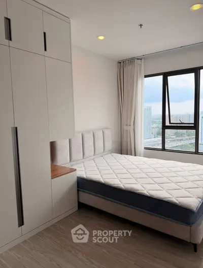Modern bedroom with large window and city view, featuring a comfortable bed and built-in wardrobe.