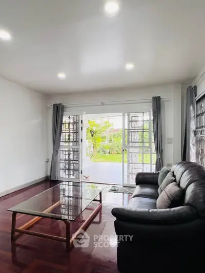 Spacious living room with garden view, featuring elegant leather sofa and glass coffee table, perfect for relaxation.