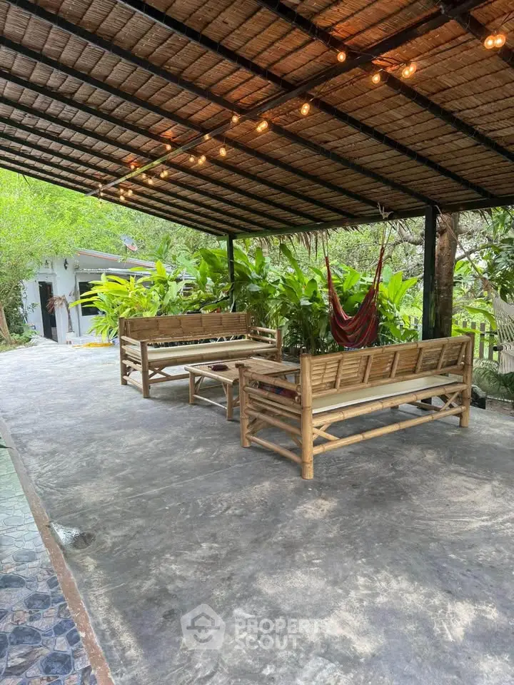 Charming outdoor patio with bamboo furniture and hammock, perfect for relaxation in a lush garden setting.