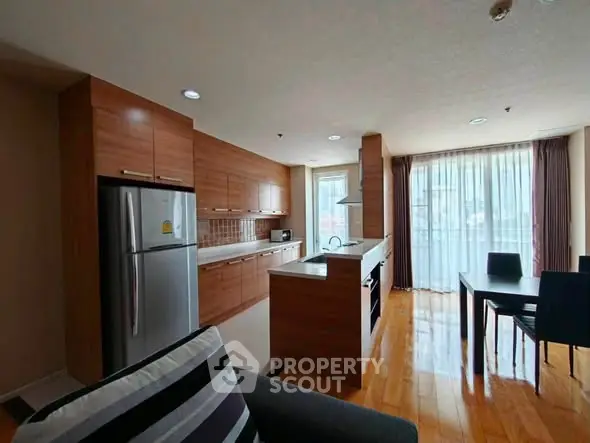 Modern kitchen with wooden cabinets and dining area in open layout apartment.