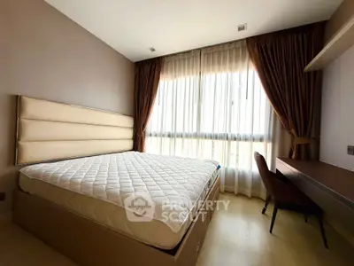 Spacious bedroom with large window and elegant curtains, featuring a comfortable bed and stylish desk.