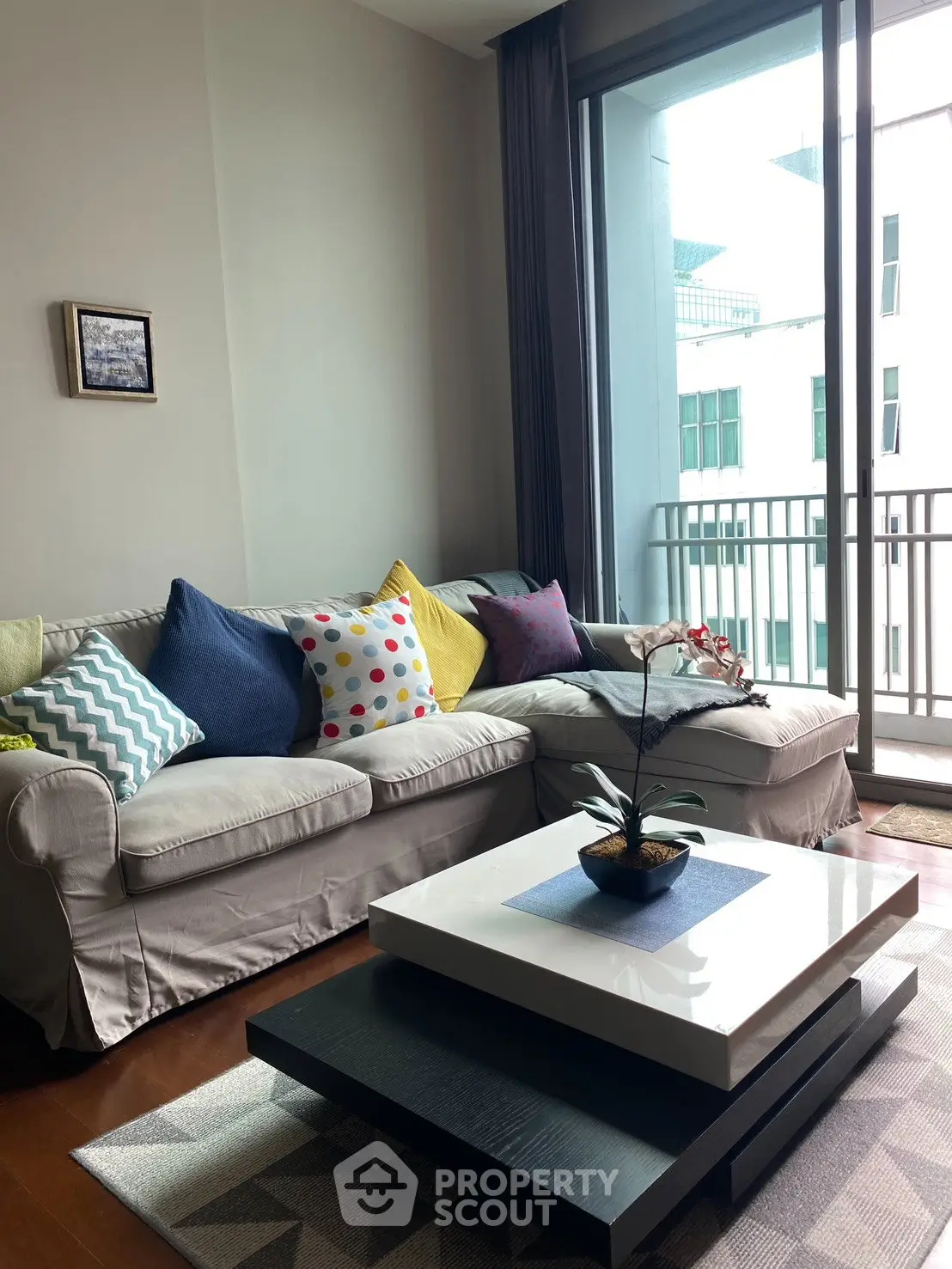 Chic living room with cozy sofa, colorful cushions, and modern coffee table near a balcony view.