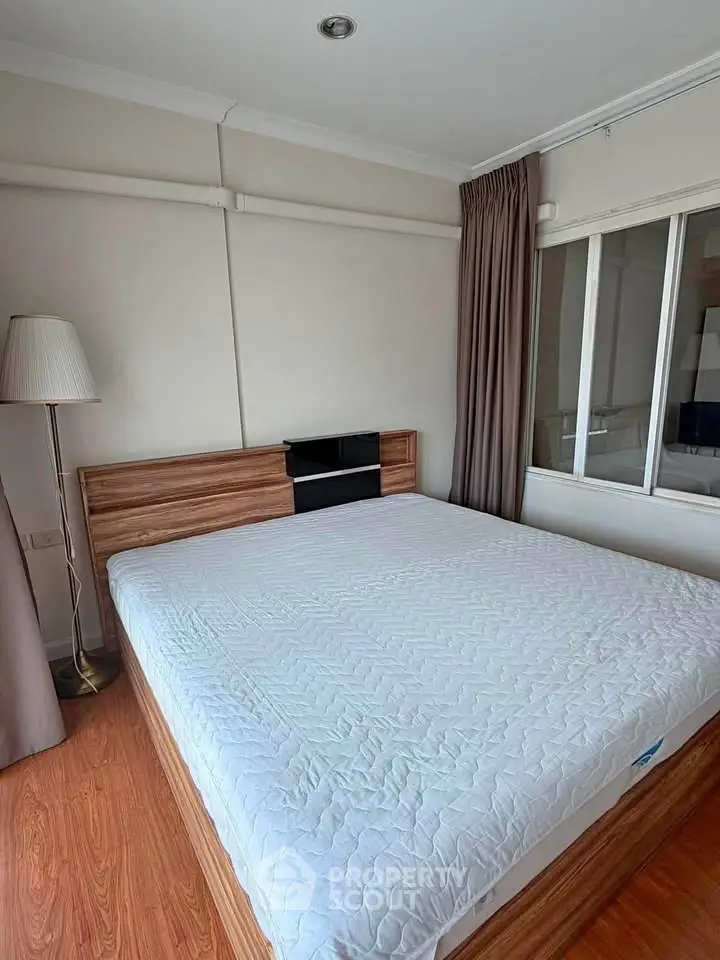 Spacious bedroom with modern wooden flooring and large window for natural light.