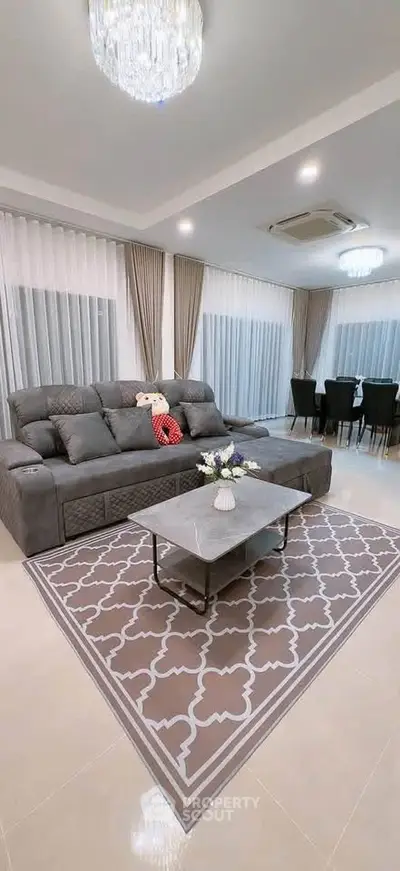 Spacious modern living room with elegant decor and dining area, featuring a plush gray sofa and stylish chandelier.