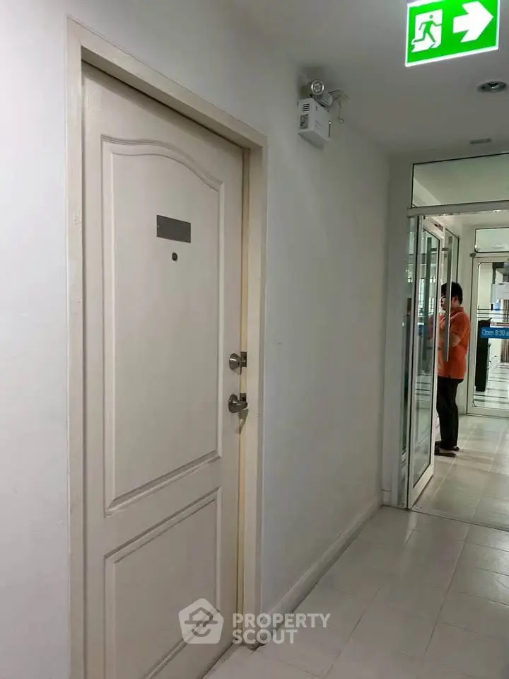 Modern apartment hallway with secure door and emergency exit sign.