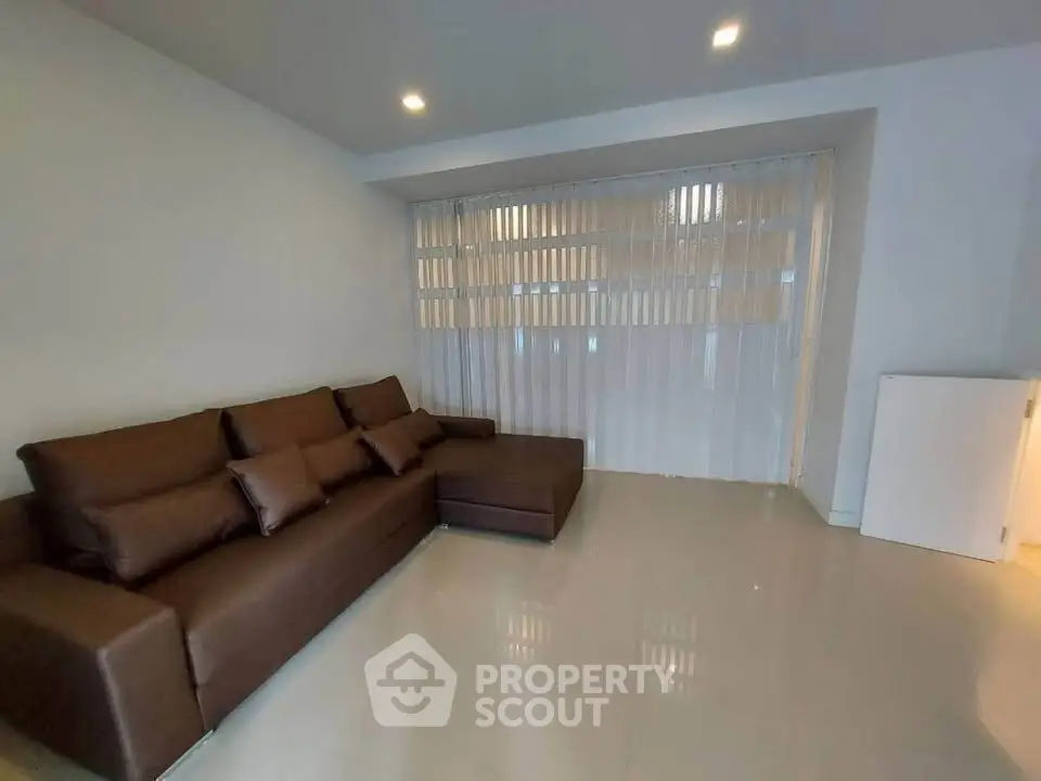Spacious living room with modern brown sofa and sleek tiled flooring, perfect for relaxation.