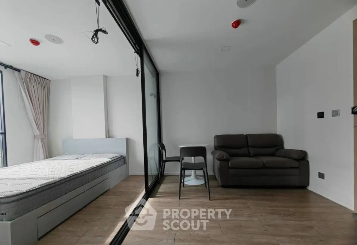 Modern studio apartment with glass partition, cozy sofa, and wooden flooring.