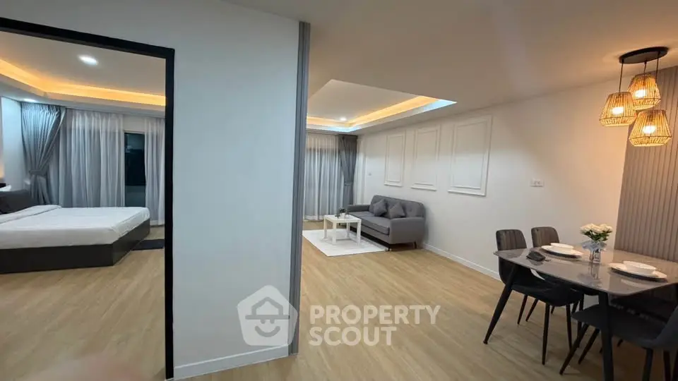 Modern open-plan living room with dining area and bedroom, featuring stylish lighting and wooden flooring.