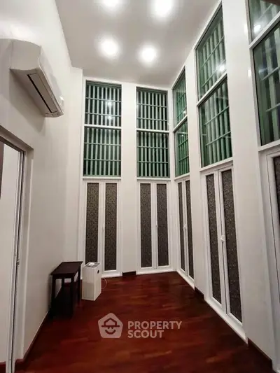 Spacious high-ceiling room with large windows and wooden flooring, perfect for modern living.