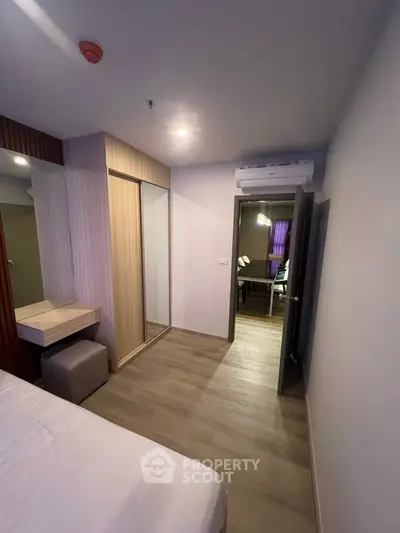 Modern bedroom with wooden flooring and built-in wardrobe, leading to a cozy living area.
