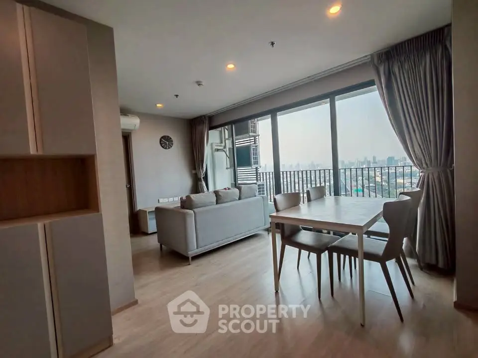 Spacious living room with large windows offering stunning city views, modern furniture, and elegant decor.