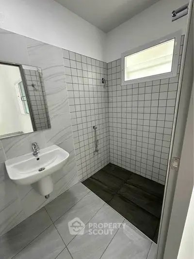 Modern bathroom with sleek tiles and minimalist design, featuring a wall-mounted sink and spacious shower area.