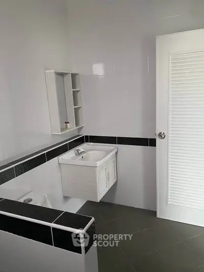 Modern bathroom with sleek white and black tile design, featuring a compact sink and storage unit.