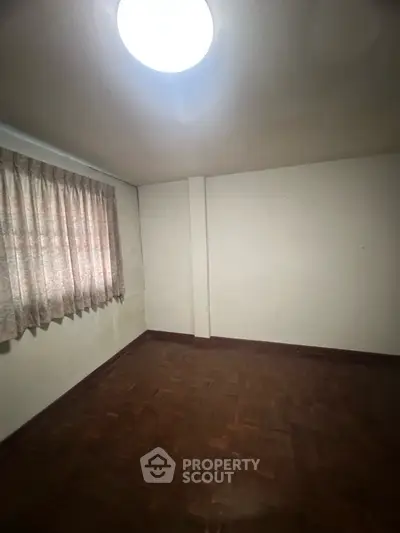 Spacious empty room with wooden flooring and natural light from window.