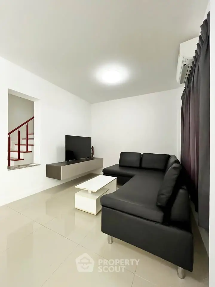 Modern living room with sleek black sofa and wall-mounted TV, perfect for relaxation and entertainment.