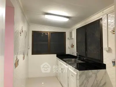 Modern kitchen with sleek black countertops and white cabinetry, featuring large windows for natural light.