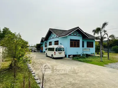 Charming single-story blue house with spacious driveway and lush greenery