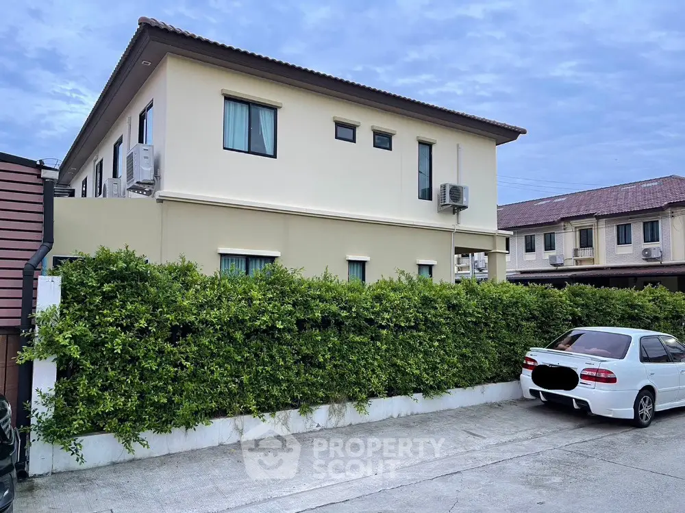 Modern two-story house with lush greenery and parked car in suburban neighborhood.