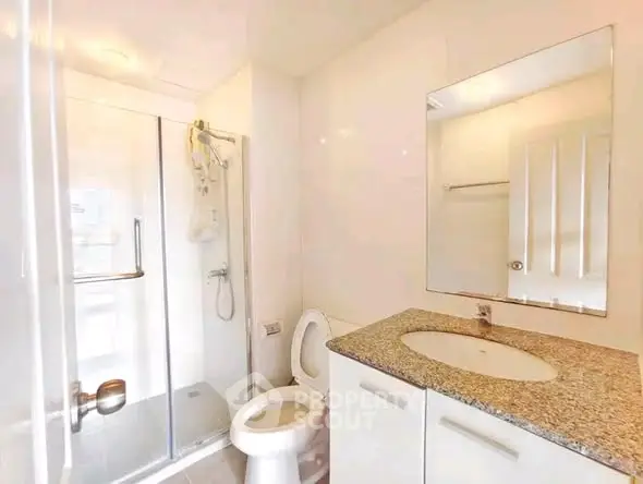Modern bathroom with glass shower and granite countertop in bright apartment.