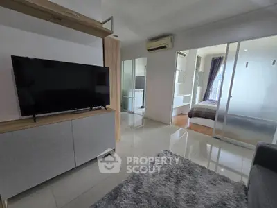 Modern apartment living room with TV and cozy rug, leading to a bright bedroom.