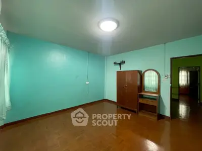 Spacious bedroom with wooden flooring and teal walls, featuring a wardrobe and vanity.