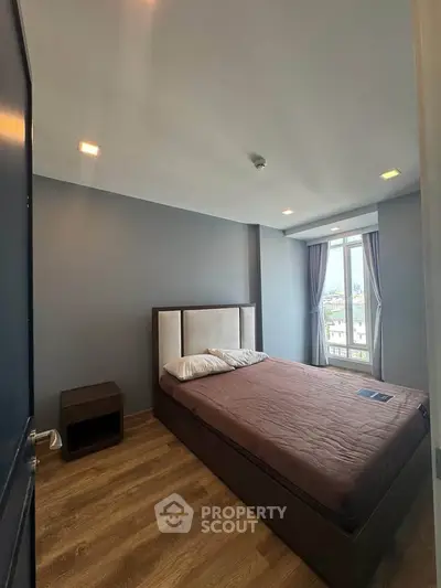 Cozy bedroom with modern decor and large window offering natural light and city views.