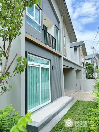 Modern two-story house with balcony and lush green lawn