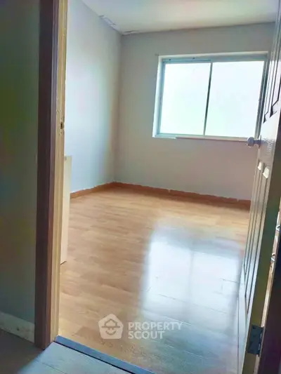 Spacious empty room with wooden flooring and large window for natural light.