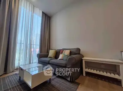 Cozy living room with modern sofa and coffee table, large window with sheer curtains.